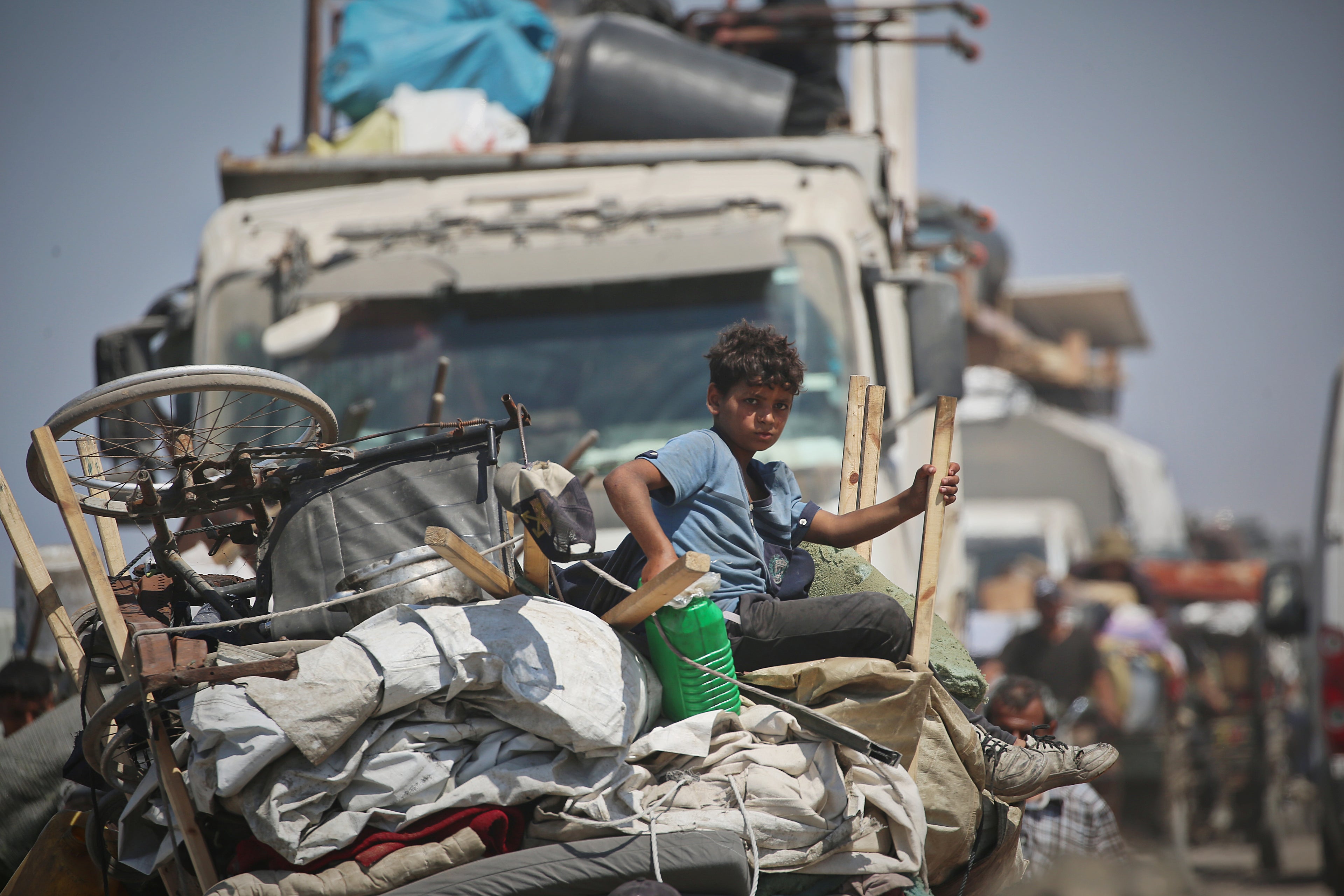 A displaced young boy sits on the back of a vehicle packed with belongings in Gaza. 