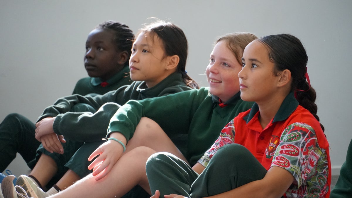 A group of four Year 6 girls in school uniform listen attentively during an LCOY held at Dubbo Zoo.