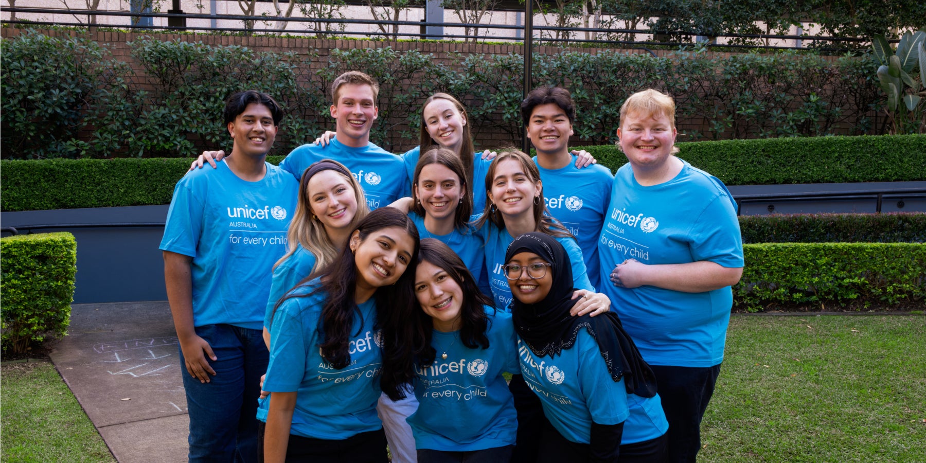 A group of 11 young people wearing UNICEF Australia t-shirts and smiling to the camera.