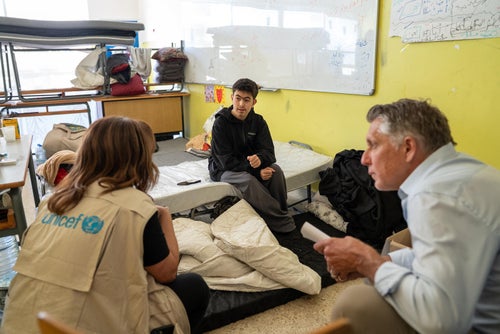 UNICEF staff talk to child sitting on school desk.