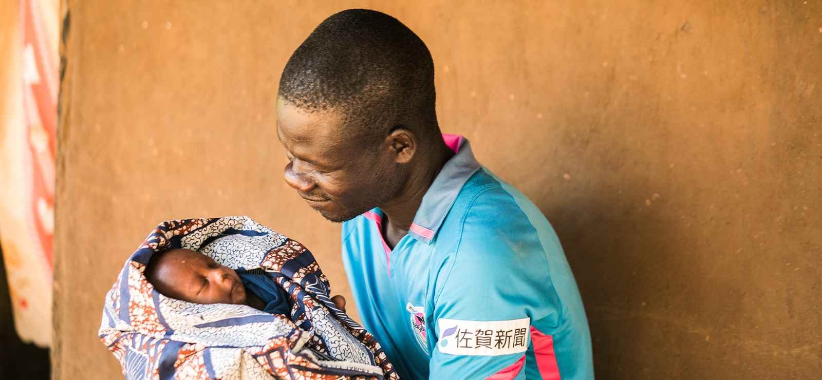 A father lovingly looks down at the sleeping baby he is holding.