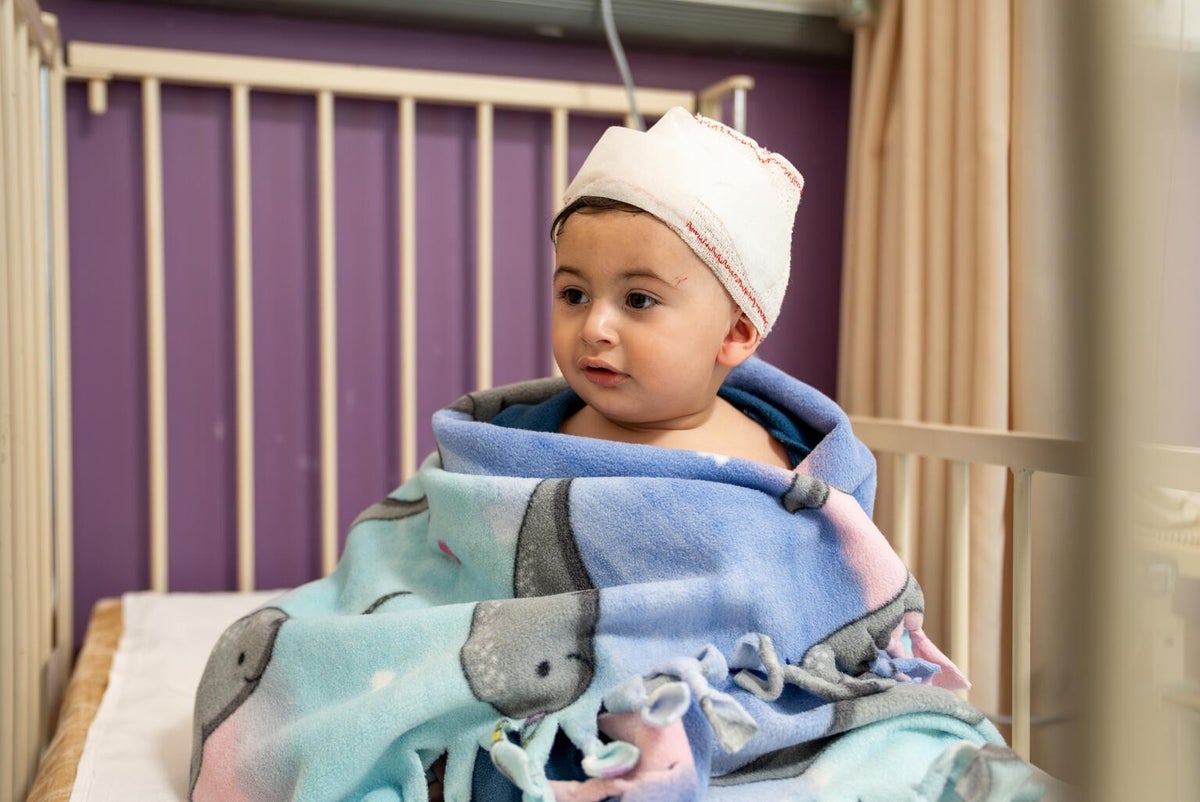 Baby wrapped in blanket sitting in hospital bed.
