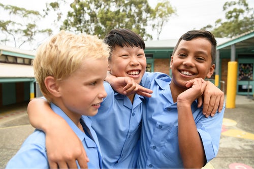 A group of three schoolboys playfully jostle in a schoolyard. 