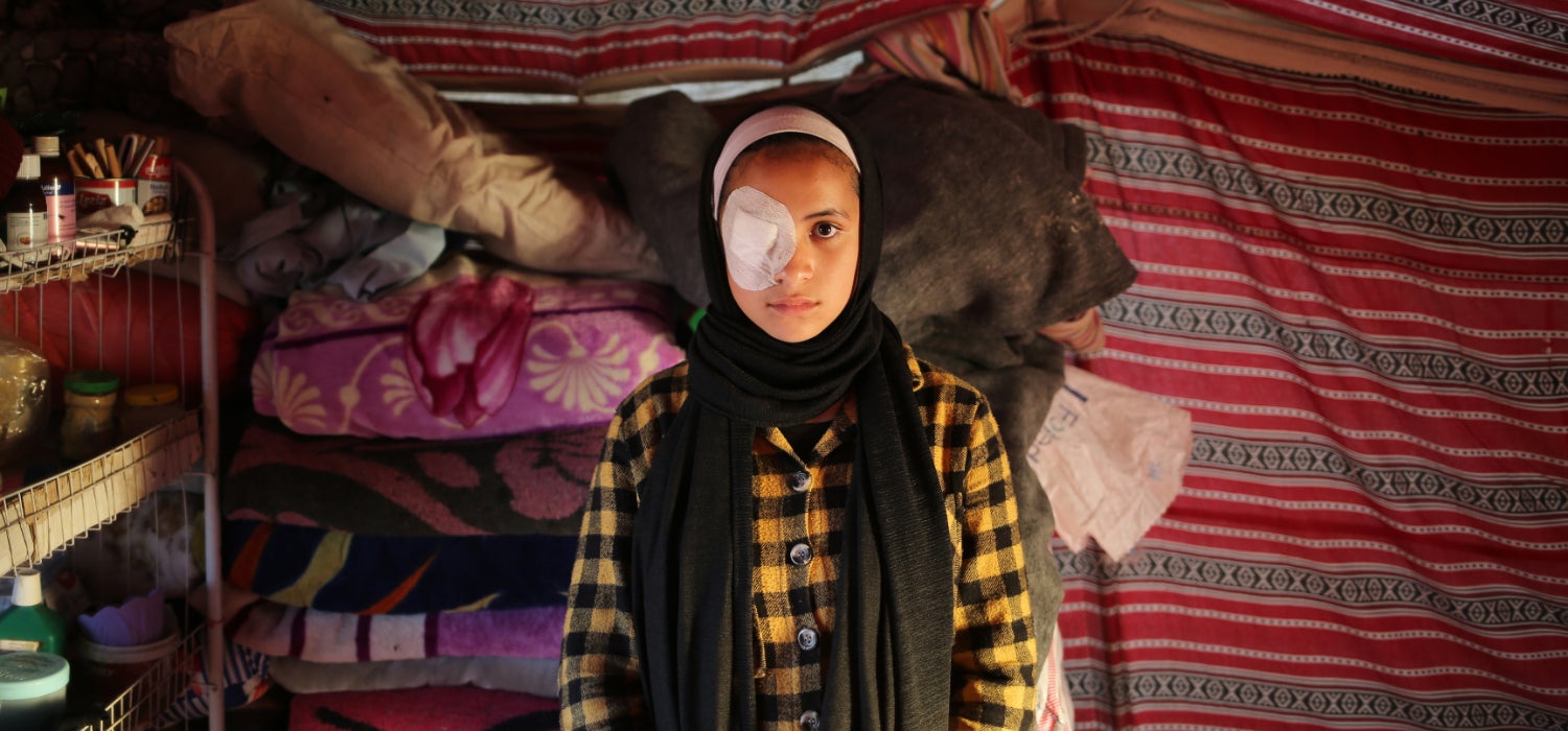 A displaced girl wearing an eye patch after her eye was damaged by shrapnel stands in her tent in the Gaza Strip. 
