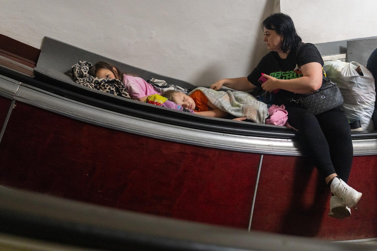 In July 2026, Maryna watches over her chidlren as they try to sleep on an escalator in a metro station where the family sought shelter from overnight attacks.