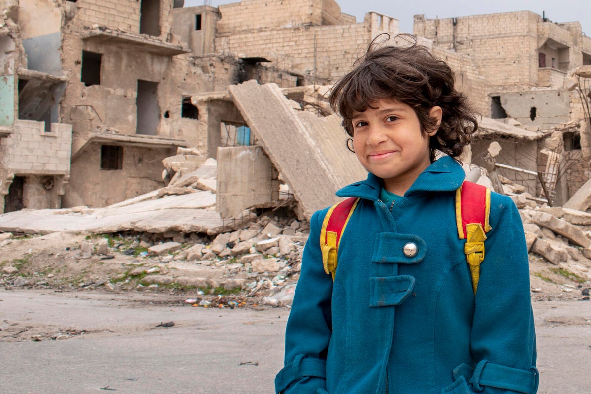 A girl stands in front of rubble. 