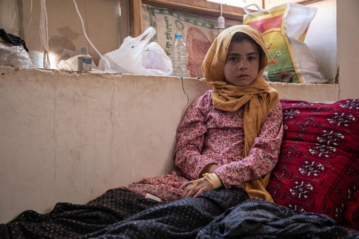 A young girl sits on a bed in a house in Afghanistan. 
