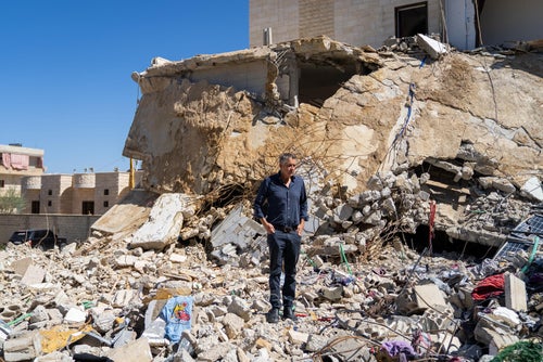 Man standing within the rumble of destroyed houses.