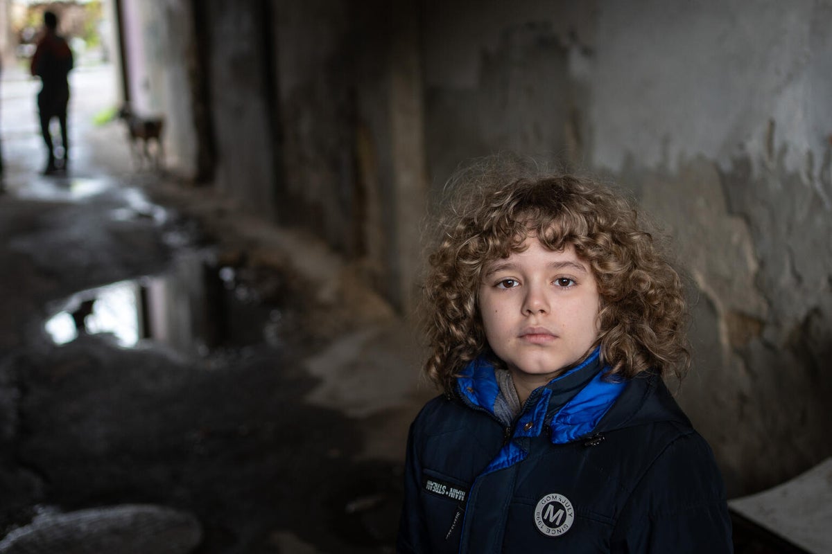 A young boy looks at the camera outside a destroyed building in Ukraine