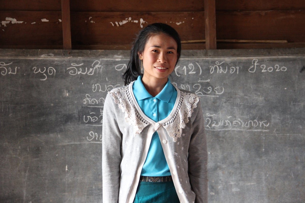 A woman standing in front of a blackboards smiles to the camera.