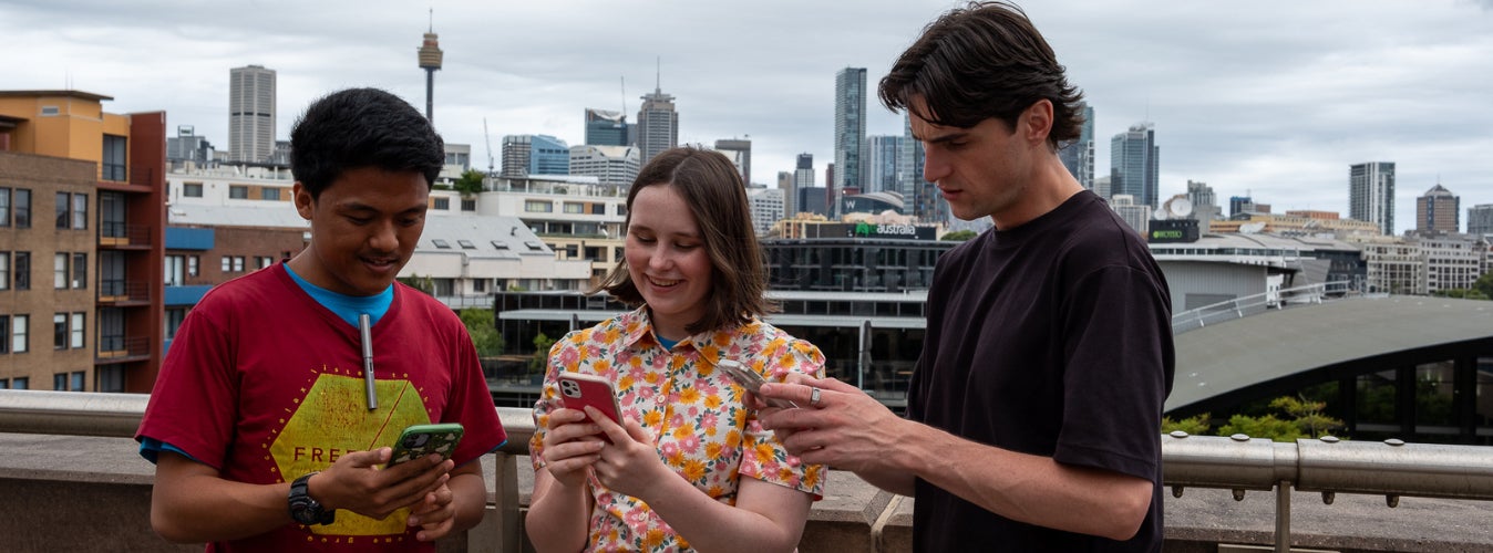 A group of three young people use their phones. 