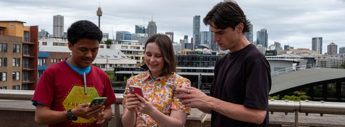 A group of three young people use their phones. 
