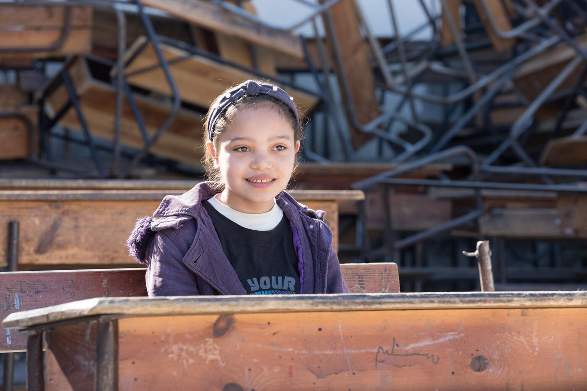 A girl sits at a desk surrounded by rubble.