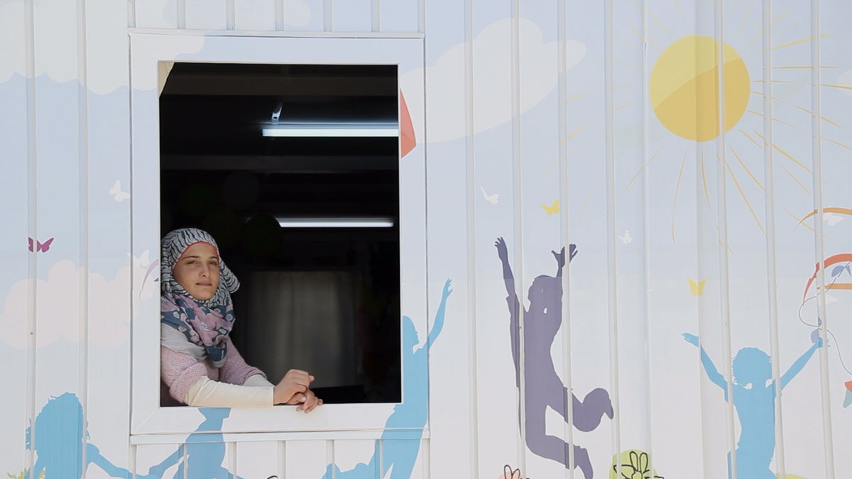 Young girls sits inside looking out the window of a UNICEF child friendly space.