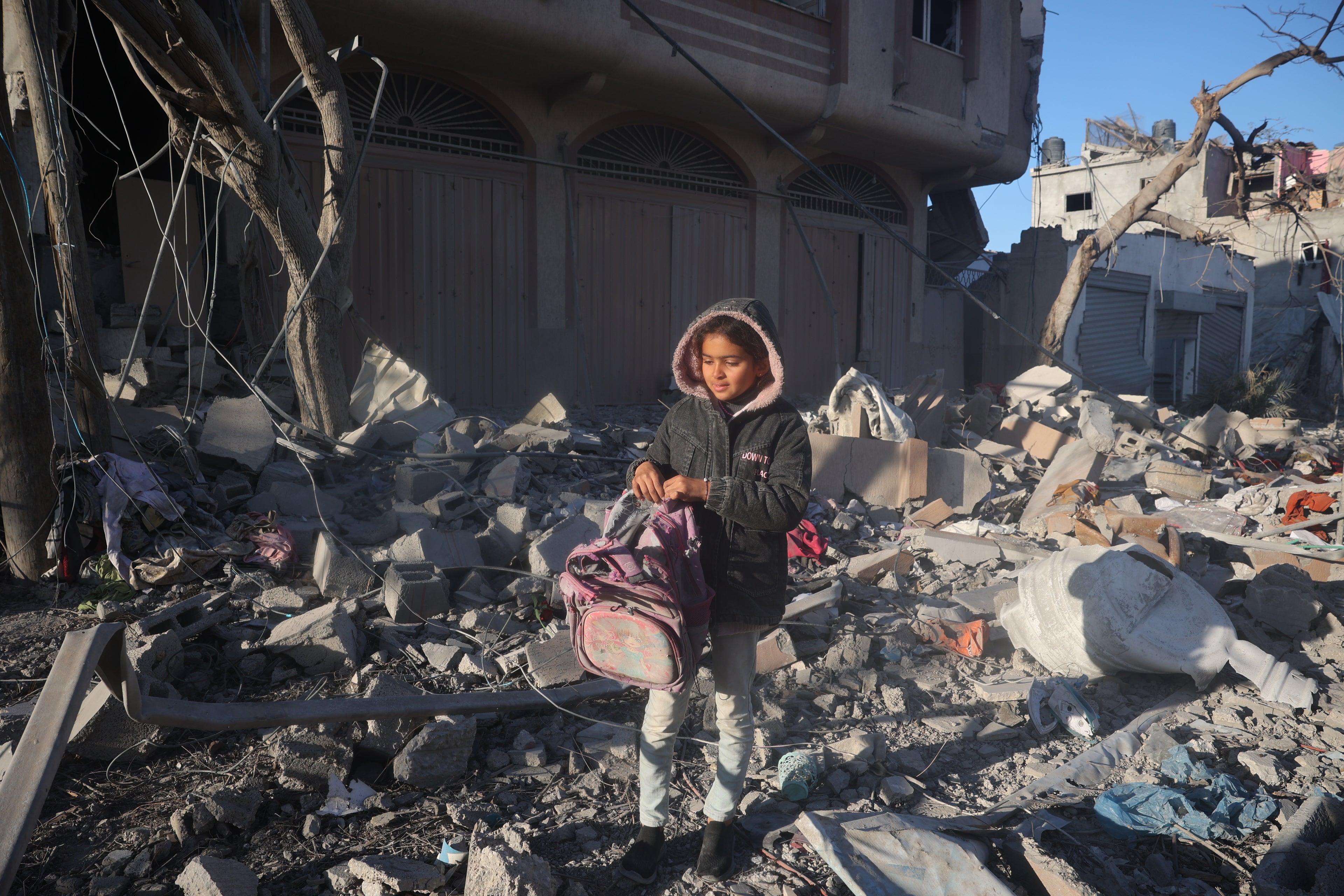 A young girl salvages a damaged backpack from the rubble of her home in the Gaza Strip. 