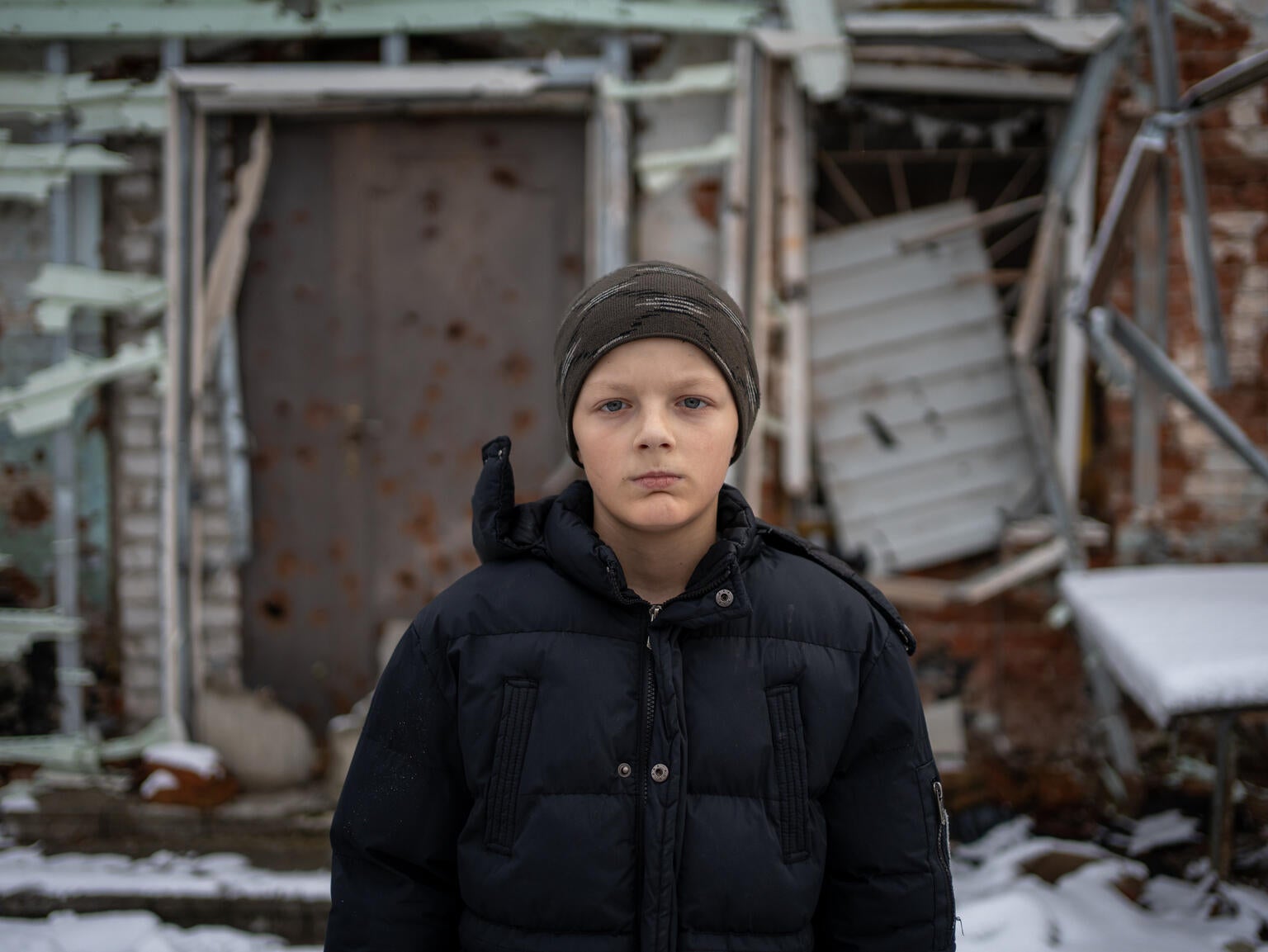 A young boy looks at the camera outside his destroyed building. 