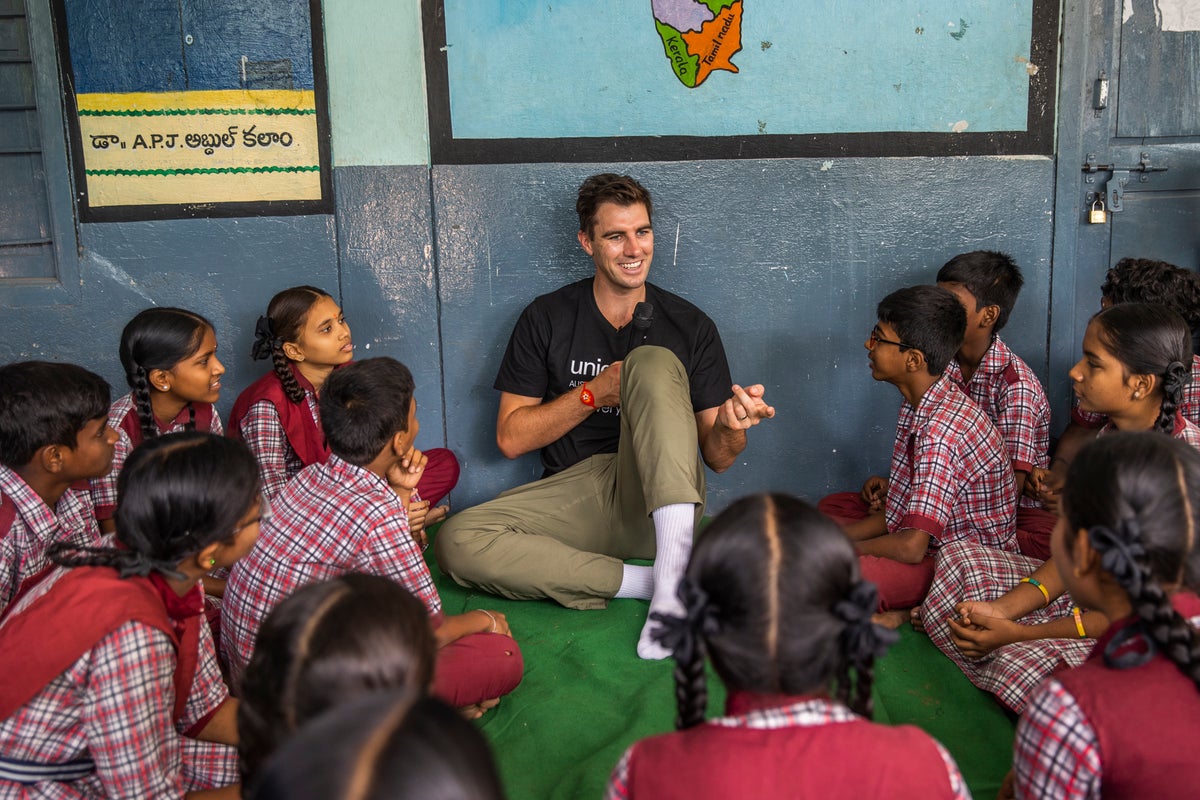 Pat Cummins sits on the ground of a classroom and speaks to a group of school children in India.