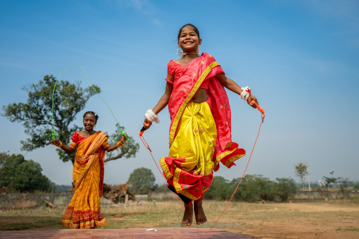 Two young girls wearing saris play with skipping ropes in a field in India. 