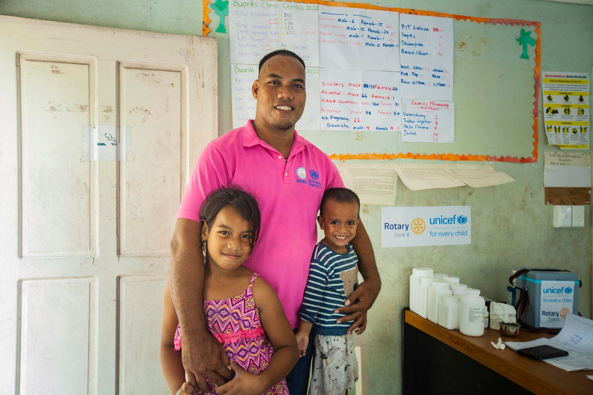 A male health worker embraces his two young children in a health facility in Kiribati. 