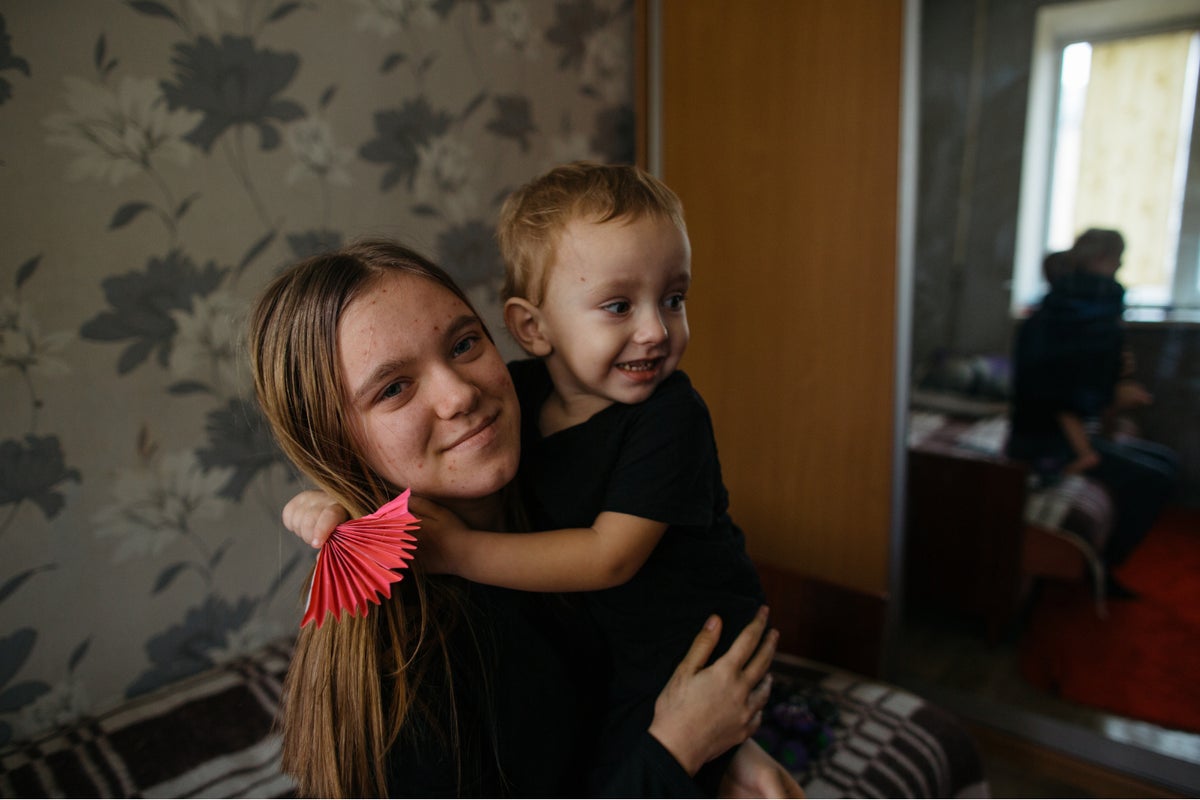 Svitlana, 14, holds her youngest brother inside the room where their family is temporarily living in Ukraine.