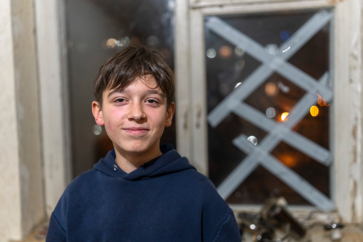 A portrait of 12-year-old Daniiel from Ukraine, with a taped up window behind him in case of attack. 