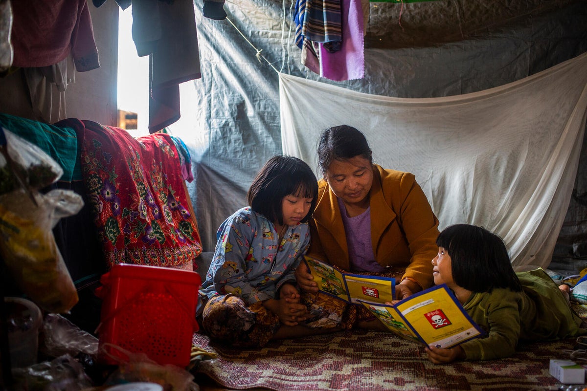 In their shelter in Shan State, a displaced mother reads a UNICEF-distributed mine risk handbook to her children. Shan has the highest civilian landmine casualties in Myanmar. 