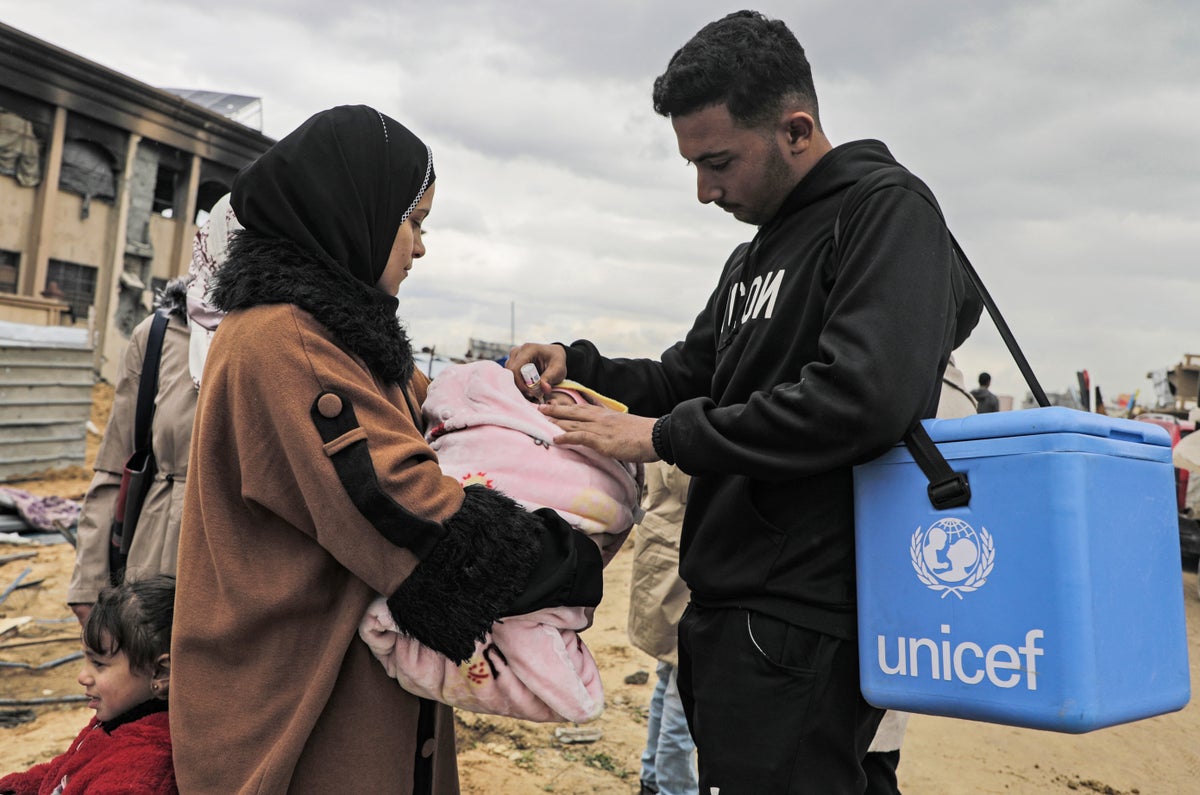 A healthcare worker gives the polio vaccine to an infant, who is being held by its mother. 