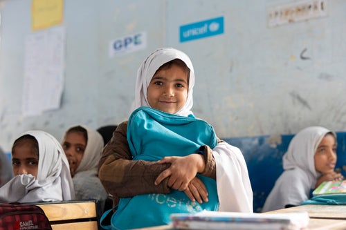 Young girl in a classroom in Balochistan tightly hugging her UNICEF backpack
