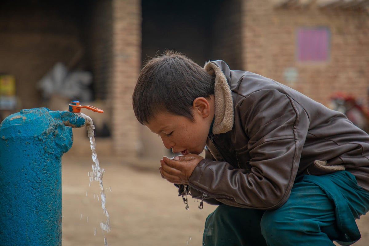 A boy drinking water from a tap.