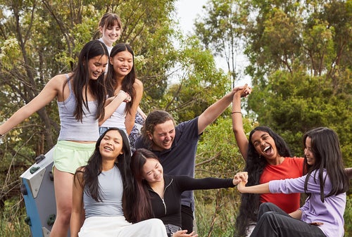 A group of smiling young people hold hands on play equipment.  