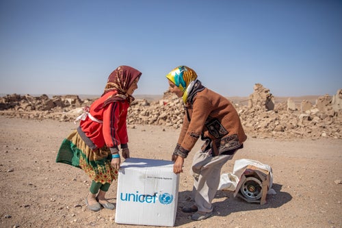 Two young girls lift a box of UNICEF supplies