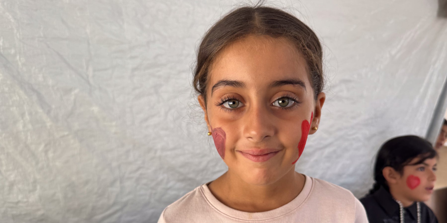 A smiling girl with facepaint stands in a UNICEF tent in Gaza.
