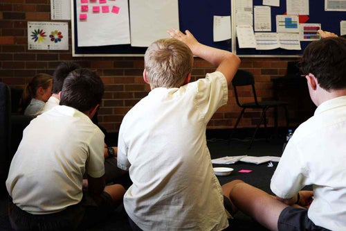 A young student raises his hand during a school lesson.