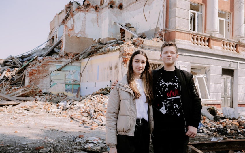 Two Ukraine children standing outside a destroyed building