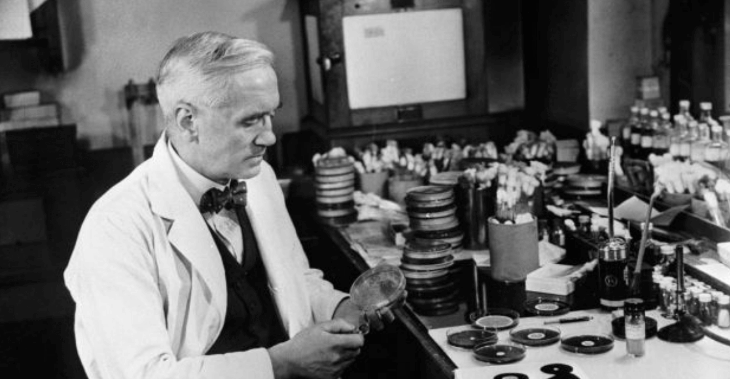 A man in a white lab coat sits at a desk with bike parts
