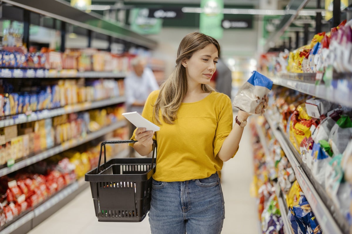 A woman in yellow looking at a bag of crackers in a grocery store