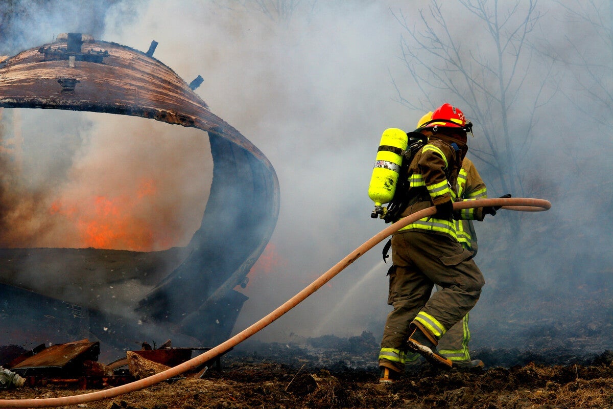 Firefighters holding a hose in a forest, fighting a wildfire