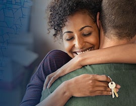 Military member hugging her spouse with new home keys in her hand.