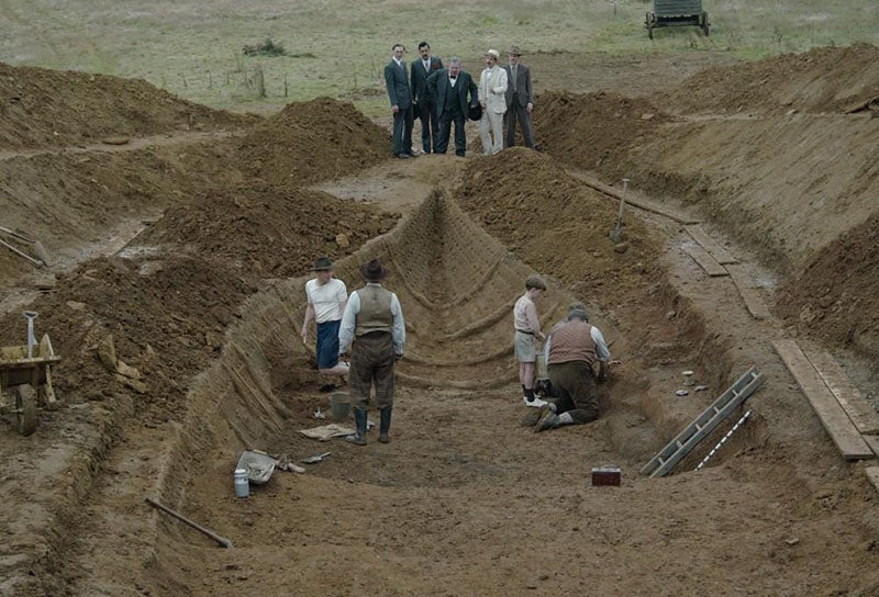 Movie still from The Dig (2021), showing impression of the Anglo-Saxon ship at Sutton Hoo, being unearthed by Basil Bown (foreground, back turned) (britishmuseum.org)