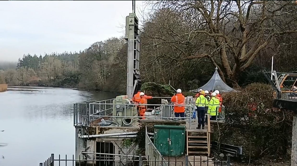 Workers in safety gear install Hydrolox water screen on the side of a river.