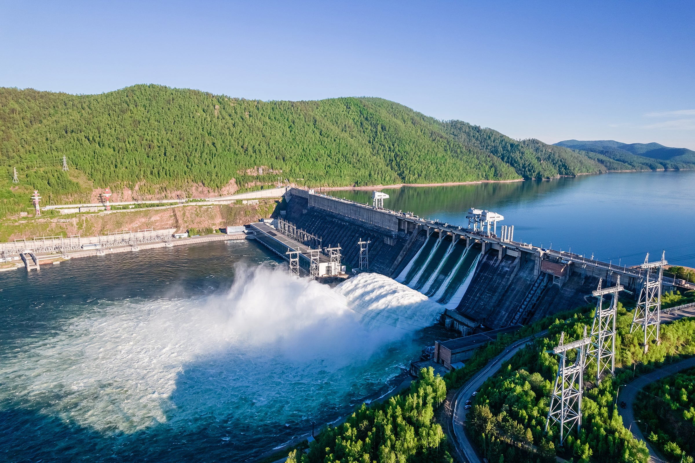 Dam on river with water flowing throw and verdant hill in background