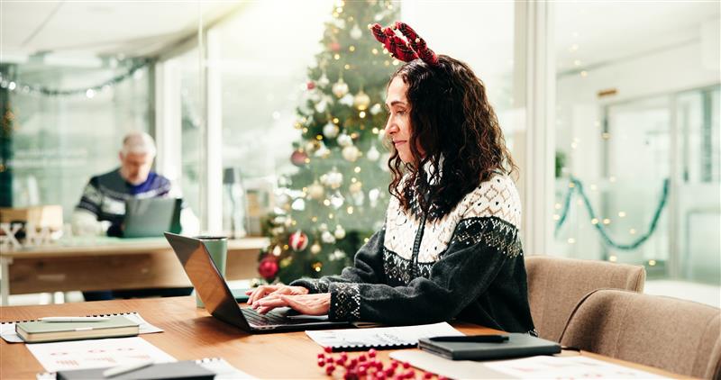 woman in holiday sweater on laptop reviewing Year-End Payroll Checklist isolved Blog