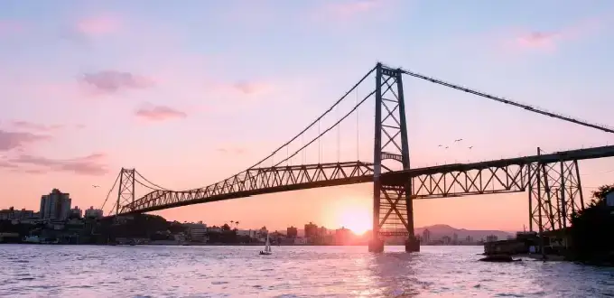 Puente Hercílio Luz en Florianópolis, Brasil, al atardecer, con el mar, barcos y el paisaje urbano de la isla.