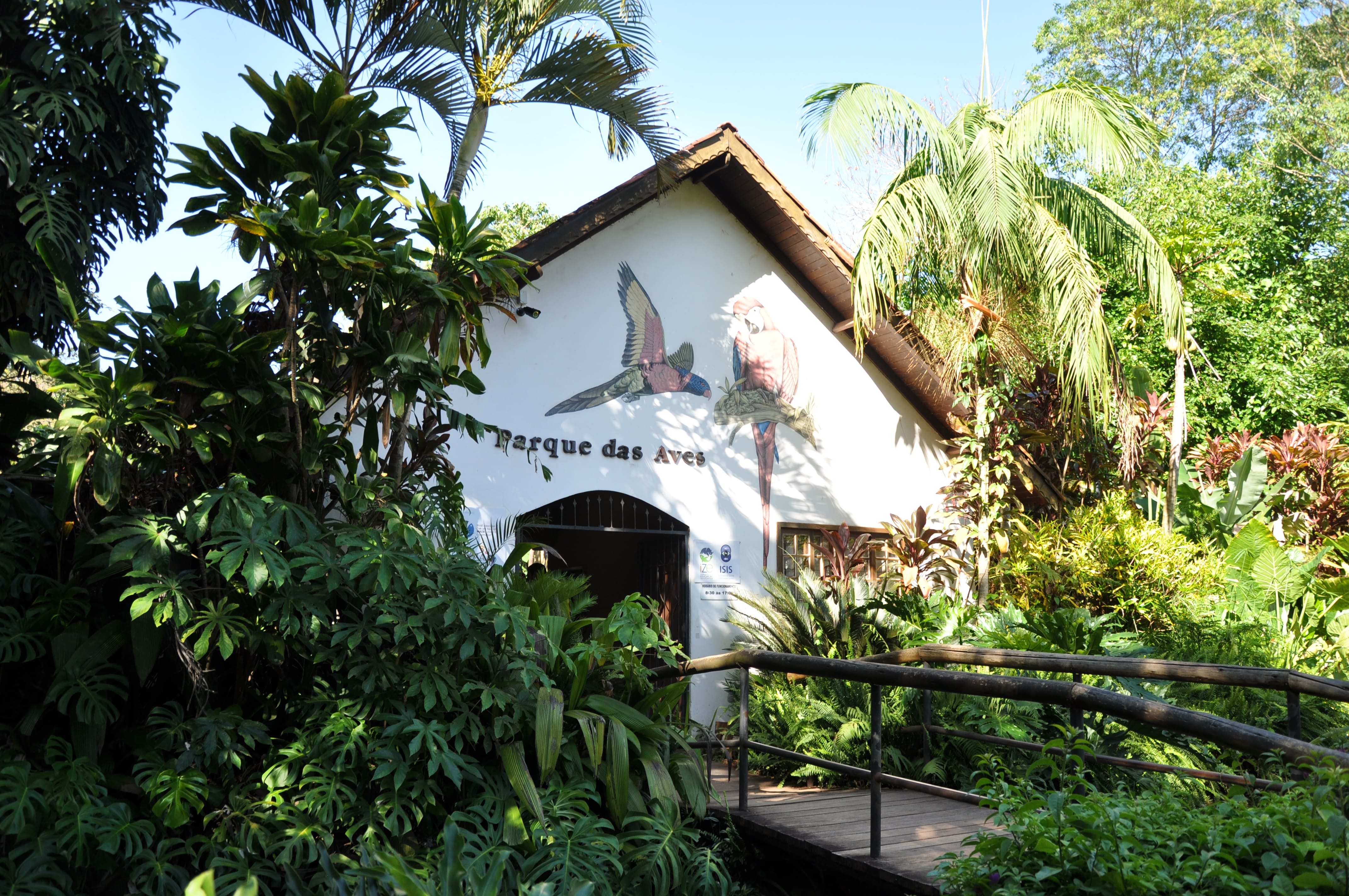 Entrada al Parque das Aves en Foz do Iguaçu, rodeada de vegetación tropical y aves pintadas en la fachada blanca.