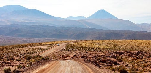 Desierto de Atacama, cerca de Calama, Chile: camino de tierra entre paisaje árido, cerros y volcanes al fondo.