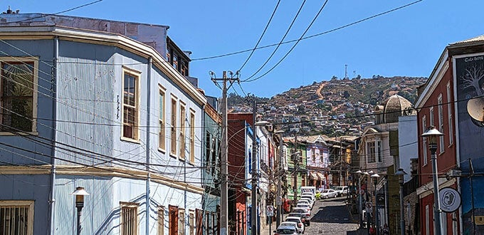 Calle empinada con casas de colores, cables aéreos y cerros poblados al fondo en Valparaíso, Chile.