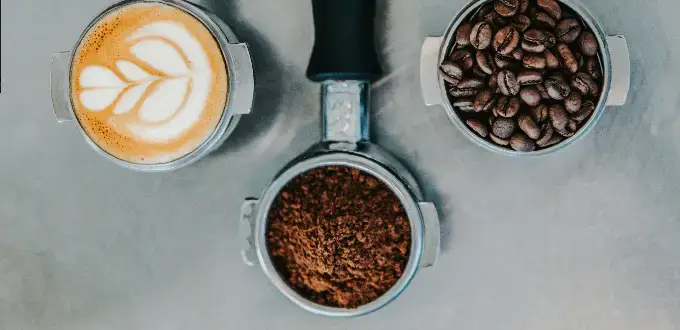 Taza de café latte con arte, granos y café molido en portafiltro, típico de cafeterías de especialidad en Ñuñoa, Santiago.