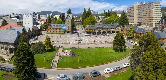 Centro Cívico de Bariloche con plaza, edificios de piedra y montañas de la Patagonia al fondo.