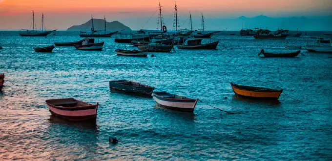 Atardecer en Búzios, Brasil, con botes tradicionales sobre el mar y vistas de la costa tropical.
