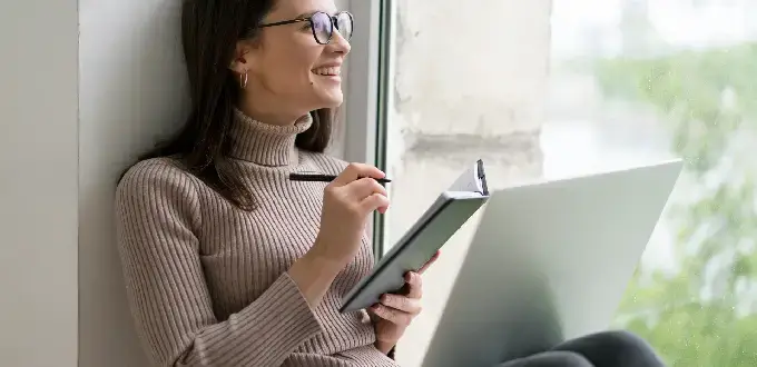 Mujer planifica su viaje a Santiago con laptop y cuaderno, organizando itinerario y vuelos desde casa.
